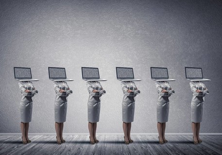 Business women in suits with laptop instead of their heads keeping arms crossed while standing in a