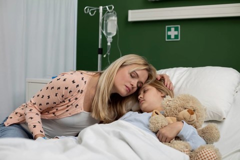 A loving mother gently comforts her sick child, who is lying in a hospital bed, creating a truly