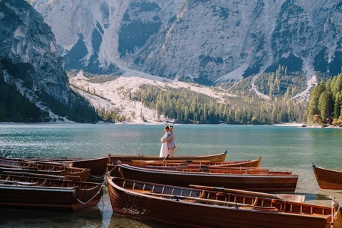 Bride and groom sailing in wooden boat, with oars at Lago di Braies lake in Italy. Wedding in