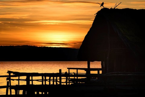 Amazing sunset landscape with a shadowed wooden hut and a bird on top of it, on a lake, at golden