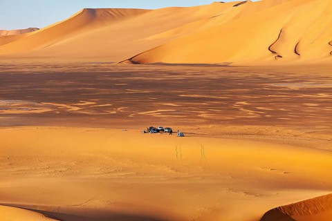 Wide sand dune landscape in yellow tones, with a small camp in the middle of the dunes, tent camp