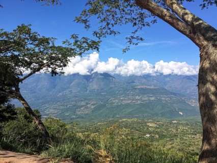 Tree framed view into a green valley and mountains with white clouds and blue sky, Barichara,