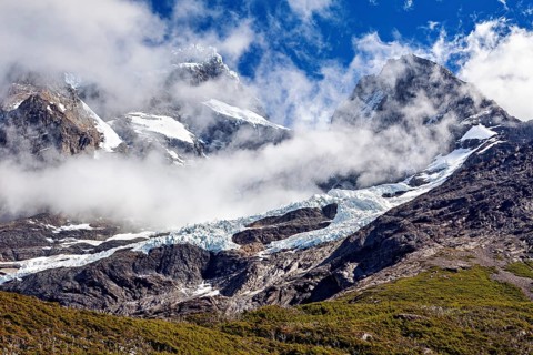 Impressive snow-covered peaks under a clear sky, framed by dramatic clouds, the glaciers of the