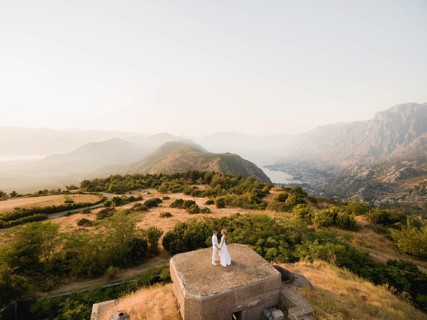 The bride and groom hold hands on the roof of the Gorazda fort, behind them a view of the Bay of