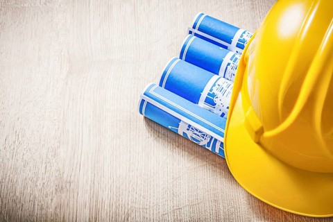 Wooden board with blue rolled construction drawings safety helmet