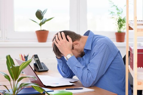 Office employee clutching his head in his hands while reading a document
