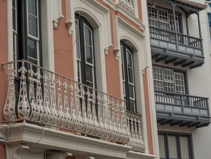 Detailed view of an old building façade with ornate balconies and windows. The colours are muted,