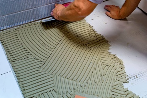 A tiler at work. Gluing floor tiles with tile adhesive and trowel. Austria