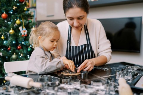 Mom puts cookie cutters on the dough next to the little girl pressing them.