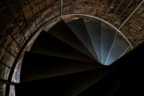 Steps of old metal spiral staircase disappear in darkness