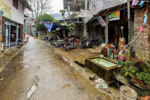 A narrow, wet road in a provincial area with parked motorbikes and colourful flags, road through a