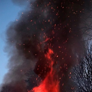 Crackling flames eat into the high pile of an Easter fire, dark smoke with flying sparks rises and