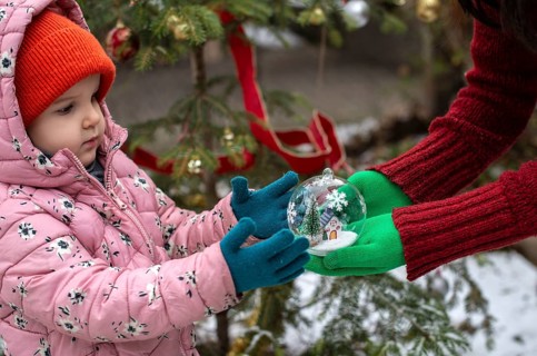 Crystal christmas ball with house and snow inside. Hands with green gloves gives transparent ball