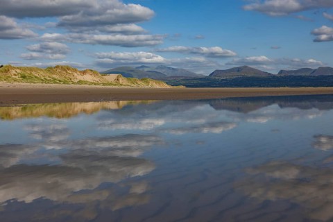 Reflection of clouds and mountains of Snowdonia National Park in the water on the beach,
