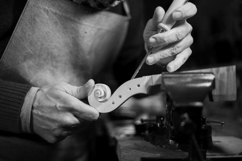 Craftsman sculpting a wooden spiral detail on a violin scroll with a chisel