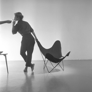 Home decor of the 1950s. A young woman is standing beside the popular Butterfly chair, also known