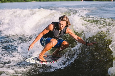 Young athletic man with long hair wakesurfing on waves of river in sunny summer weather. Ttheme