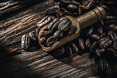 Wholegrain coffee seeds in scoop on wooden board