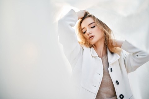 Young attractive woman in white clothes posing on abstract pale background looking at camera