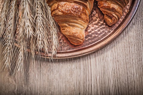Composition of wheat rye ears freshly baked croissants Copper tray on wooden board