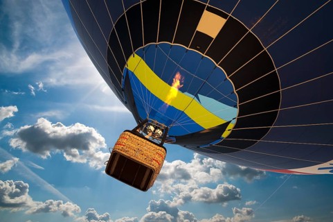 Hot air balloon with gondola in front of a blue sky with white clouds