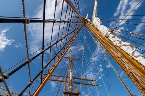 Low angle view of sailboat wooden ship masts and rigging under blue sky with clouds