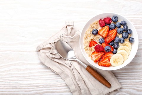 Oatmeal porridge with fruit and berries in bowl with spoon on white wooden background table top