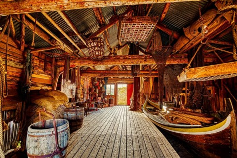 A wooden interior features tightly packed fishing equipment and a small boat, suggesting a seashore