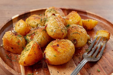 Half-eaten fried new potatoes, with butter and dill, on a wooden plate, with a fork, at home,