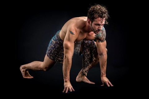 Handsome shirtless muscular man in briefs, covering with long elegant scarf, kneeling, isolated on