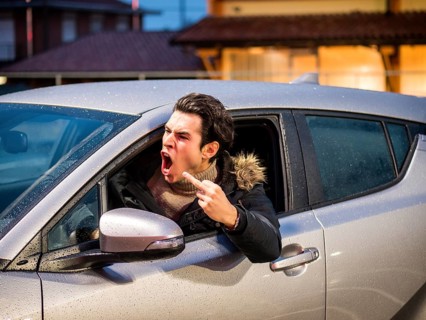 Aggressive man driving car and screaming away while showing obscene gesture on street
