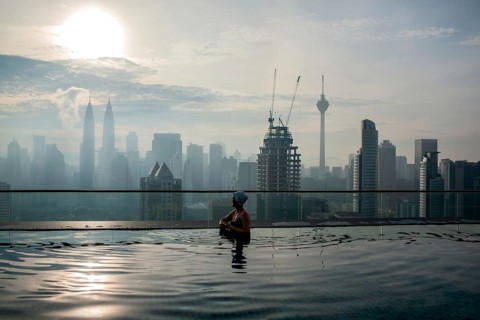 Woman enjoying cityscape of Kuala Lumpur from rooftop swimming pool. Urban scene with skyscrapers,