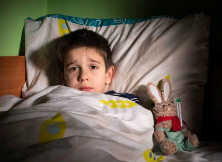 Sick child in bed with teddy bear. Measuring the temperature with a thermometer
