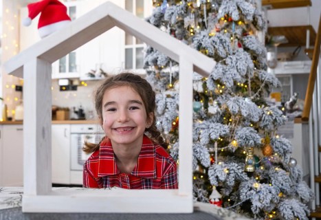 Happy child with tiny house in cozy home with Christmas decor of festive white kitchen. Gift for
