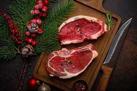 Two raw uncooked meat beef steaks on wooden cutting board with knife and seasonings on dark rustic