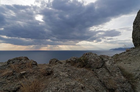The rays of the sun over the sea make their way through the clouds.Cape Meganom, Crimea,