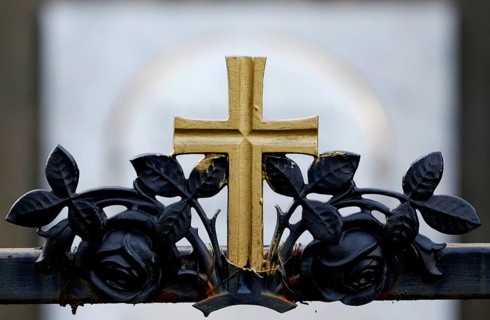 Golden cross on a wrought-iron fence of a grave in a cemetery