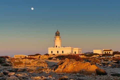 A view of the Cap de Cavalleria Lighthouse on Menorca at sunset with a full moon rising