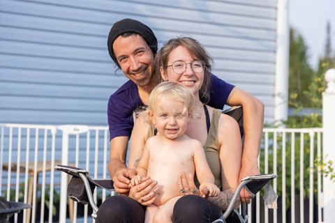 Happy young family pose for group portrait seen from the front. Mother sitting on chair with two