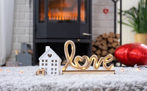 Key to house with keychain against background of fireplace stove with fire and firewood in
