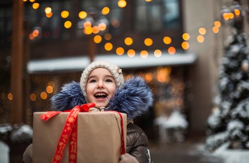 Portrait of joyful girl with a gift box for Christmas on a city street in winter with snow on a