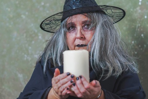 Old white-haired white-haired witch dressed in black with a hat and a large white candle in her