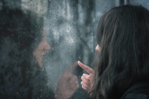 Brunette young woman and her reflection on a window covered with raindrops