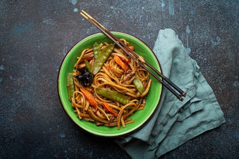 Asian dish stir fry udon noodles with chicken, vegetables and mushrooms in green ceramic bowl with