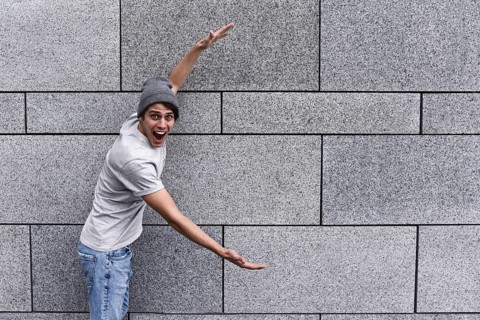 Cheerful guy dressed in gray t-shirt, sunglasses and hat at the street, show a big sale, or nice