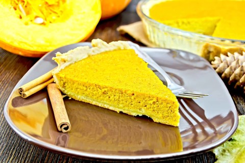 A piece of pumpkin pie in a brown plate with a fork and cinnamon, pumpkin, cones and maple leaf on