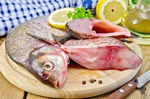Bream whole peeled and sliced pieces on a round board, parsley, lemon, vegetable oil, napkin, knife