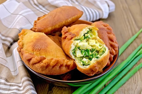 Dish with fried patties with onions and egg, napkin, a bunch of spring onions on a wooden boards