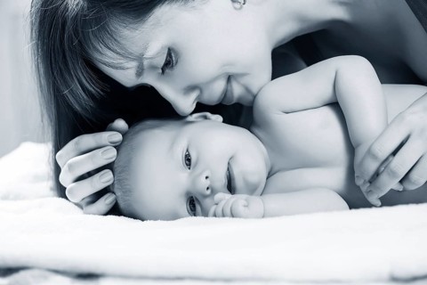 Closeup portrait of cheerful young mother with adorable newborn baby having fun at home, child
