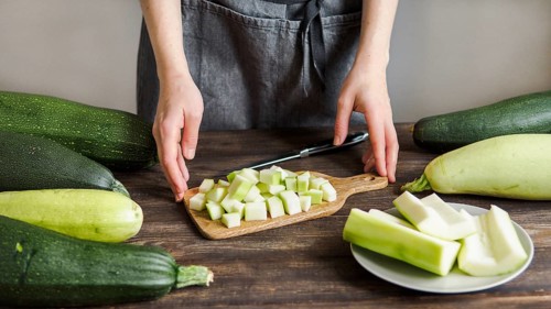 Zucchini harvest. Woman slices zucchini cubes for freezing on wooden table. Farm organic zucchini